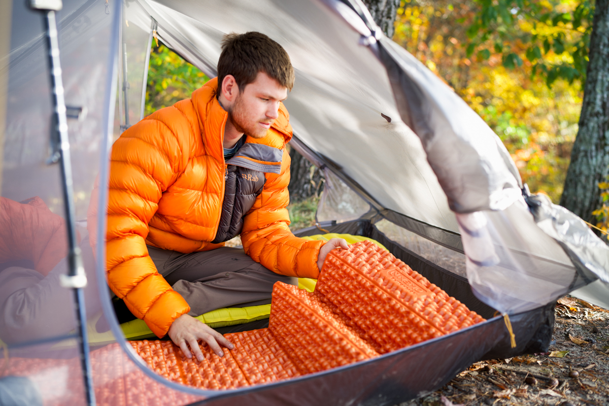 A man unfolding an orange foam pad in a backpacking tent