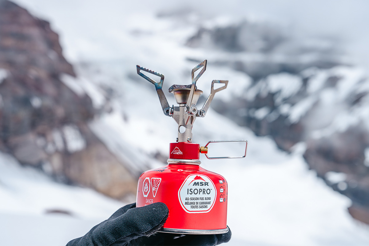 Holding up a backpacking stove and canister in snowy landscape